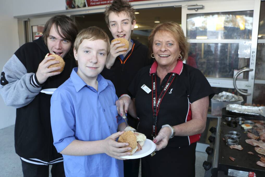 TUCK IN: YMCA Breakfast Club co-ordinator Leonie Ralph serves up bacon and egg rolls for students, from left, Mark Mougios, 16, Jake Cowan, 13, and Jake's brother Aayden Cowan, 14, on Wednesday. Picture: David Stewart