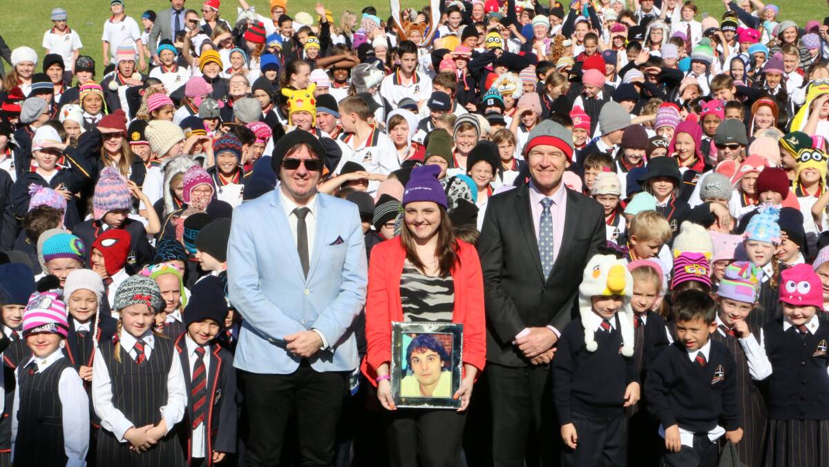 BEANIE PARADE: Bec Marcuccio holds a picture of her late husband, Rocky. She is flanked by her friend and teacher Chris Botfield, left, and school principal Michael Hannah, and dozens of Lakes Grammar junior students and staff. Pictures: David Stewart