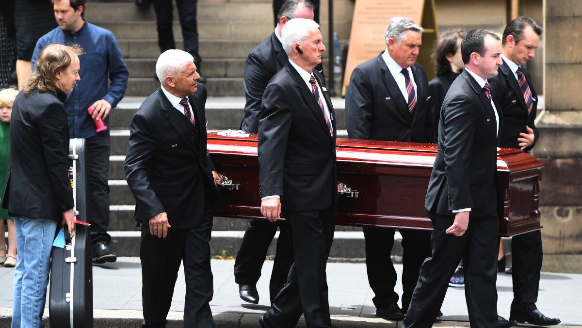 Angus Young (left) holds a guitar as the casket of his brother AC/DC co-founder and guitarist Malcolm Young is carried to a hearse in Sydney on Tuesday. Picture: Dean Lewins