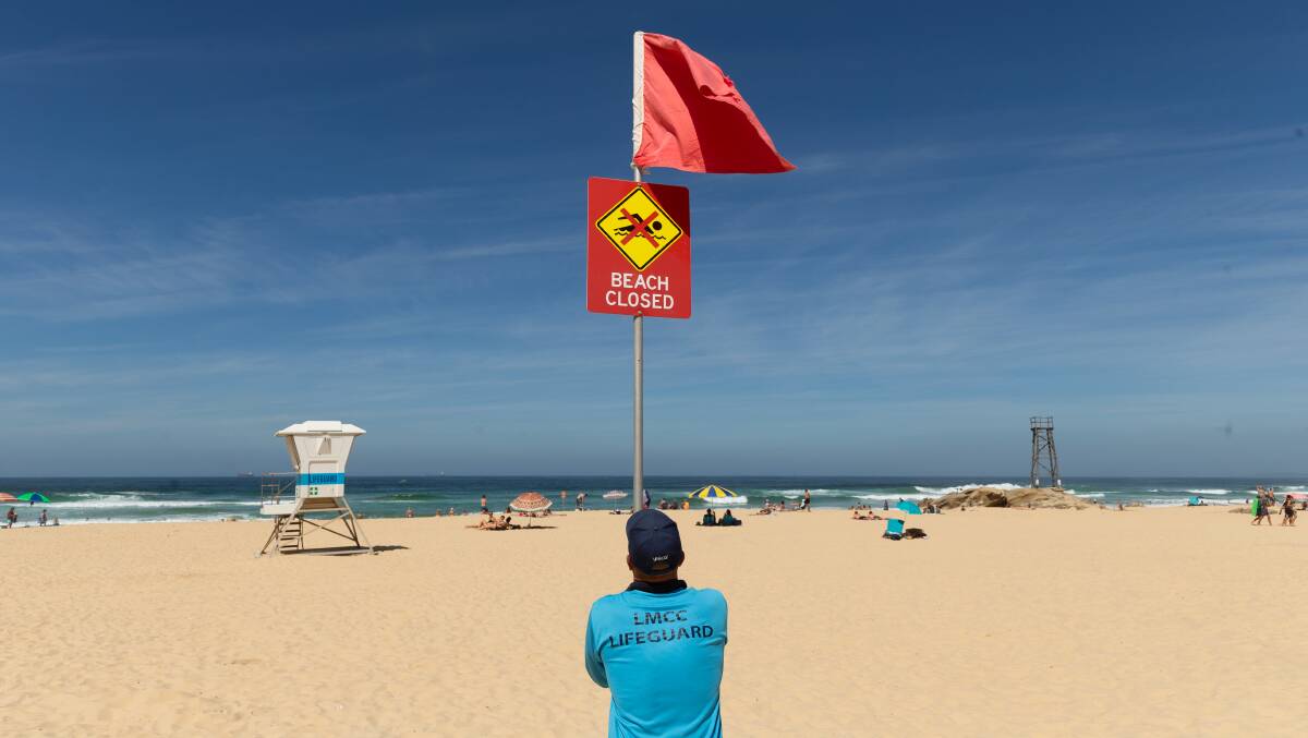 SHUT DOWN: A lifeguard erects signs at Redhead Beach after Lake Macquarie City Council closed its beaches in response to the COVID-19 crisis. Picture: Max Mason-Hubers.