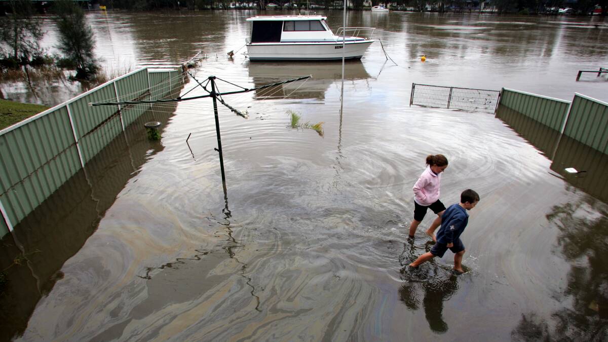 OVERFLOWING: Children trudge through the yard of a Dora Creek home during the flood of 2007. Some residents in the town want council to do more to reduce the threat from the next flood. Picture: Kitty Hill