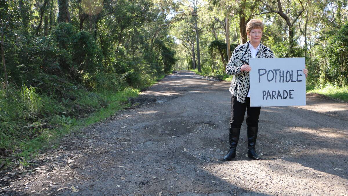 VEHICULAR MINEFIELD: Wangi Wangi resident Jenny King stands in a Reserve Road pot-hole with a sign created by a local wag. Picture: David Stewart