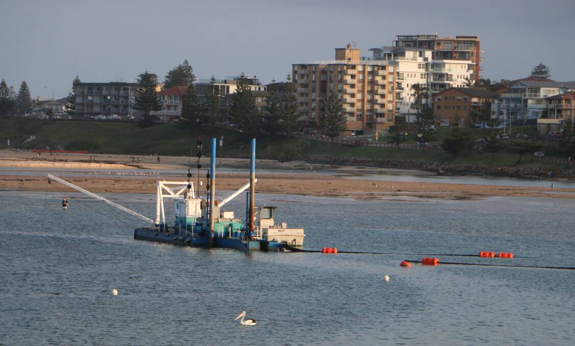 READY TO GO: The sand dredge in place at The Entrance on Saturday night. Dredging is due to start this week. A man can be seen walking in the shallow water behind the dredge. Picture: David Stewart